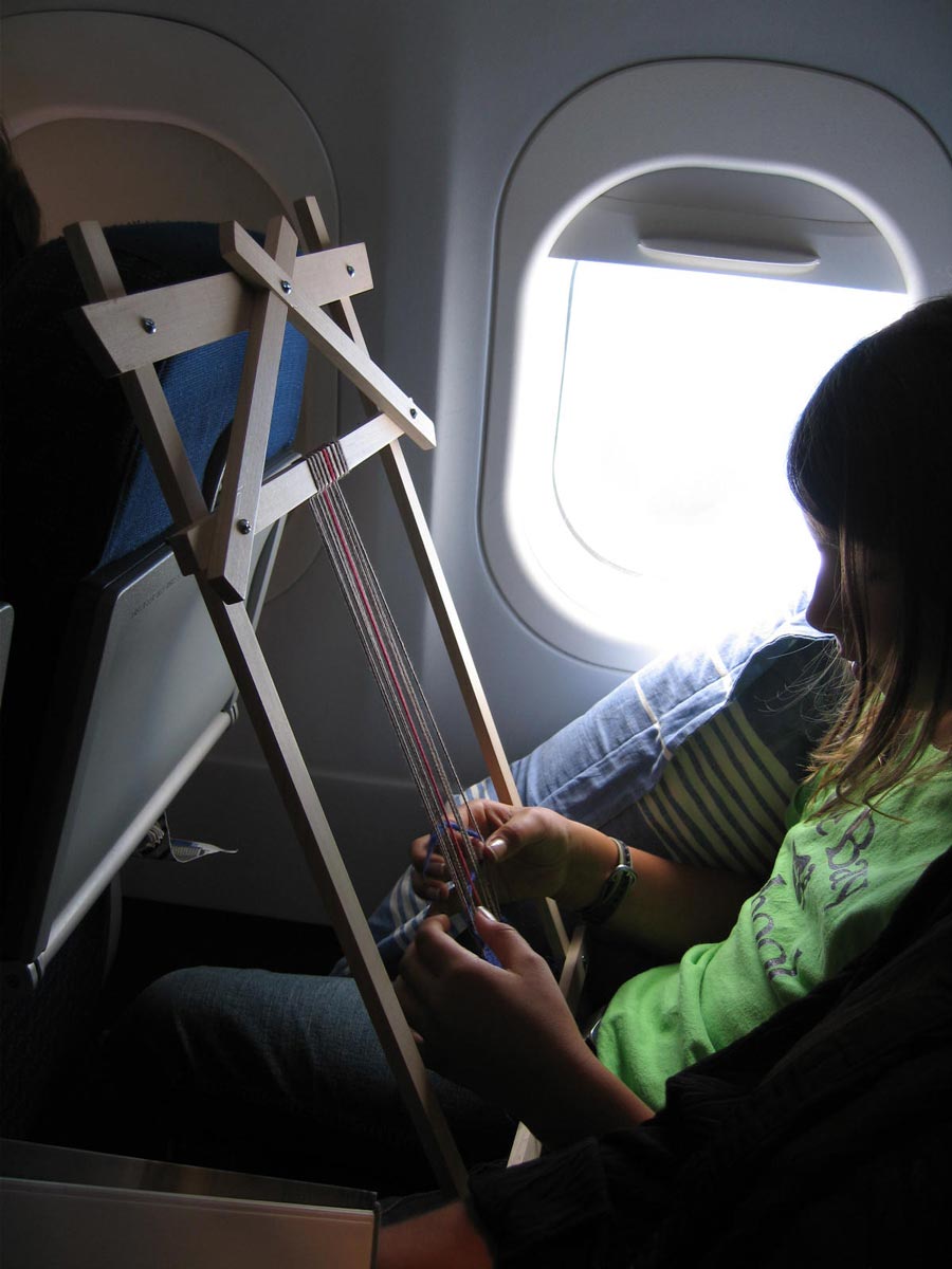 girl weaving on small loom on airplane