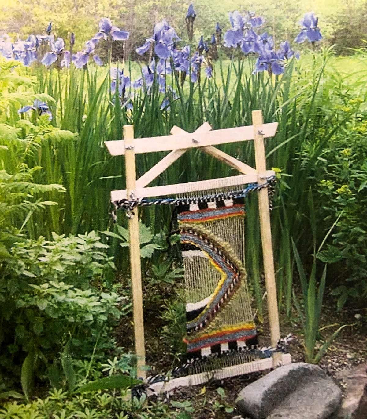 small loom with weaving on it standing up in front of plants